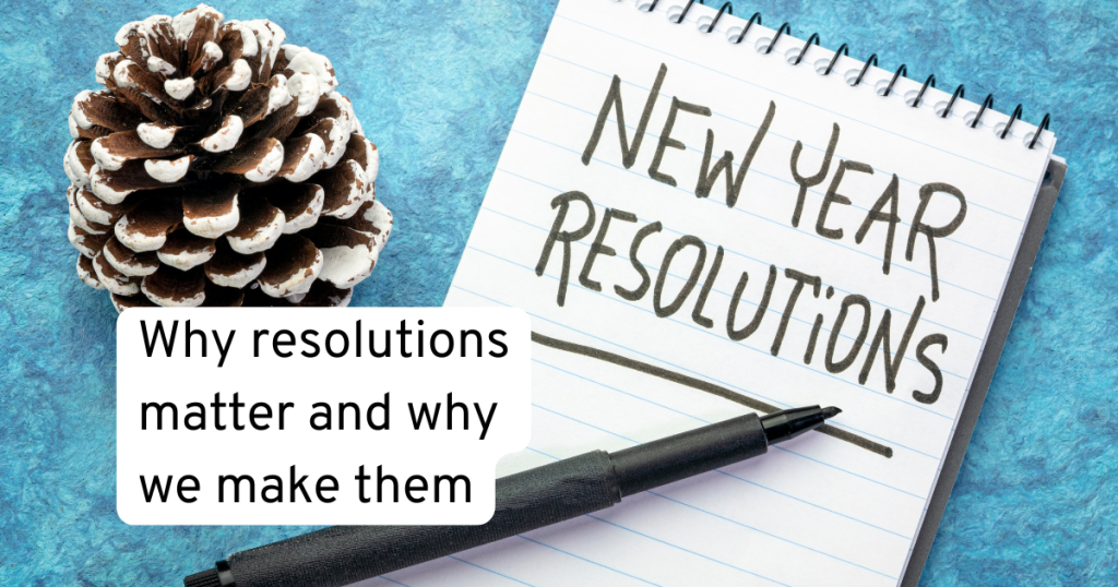 note pad on a blue background with a silver sprayed pine cone symbolling the end of christmas and text on the notepad which says new year resolutions with a pen. reminding us why we make resolutions