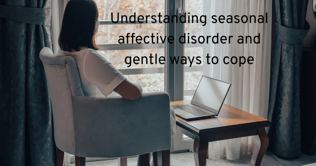 WOMAN LOOKING OUT OF HER WINDOW AT A LAPTOP TRYING TO UNDERSTAND SEASONAL AFFECTIVE DISORDER AND GENTLE WAYS TO COPE